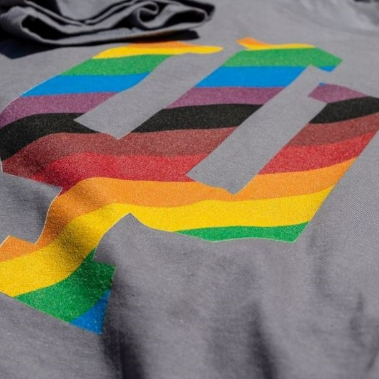 A grey shirt with a trident in rainbow coloring.