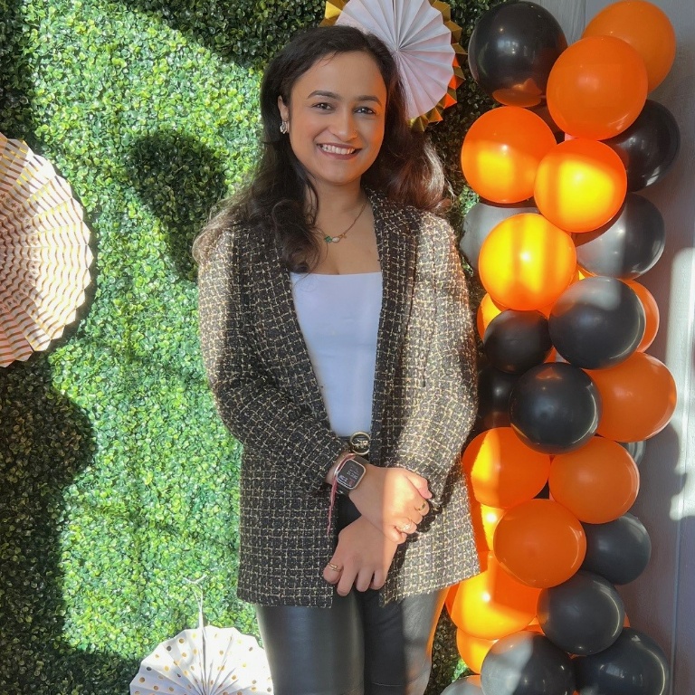 A woman stands smiling in front of balloons and a green wall.