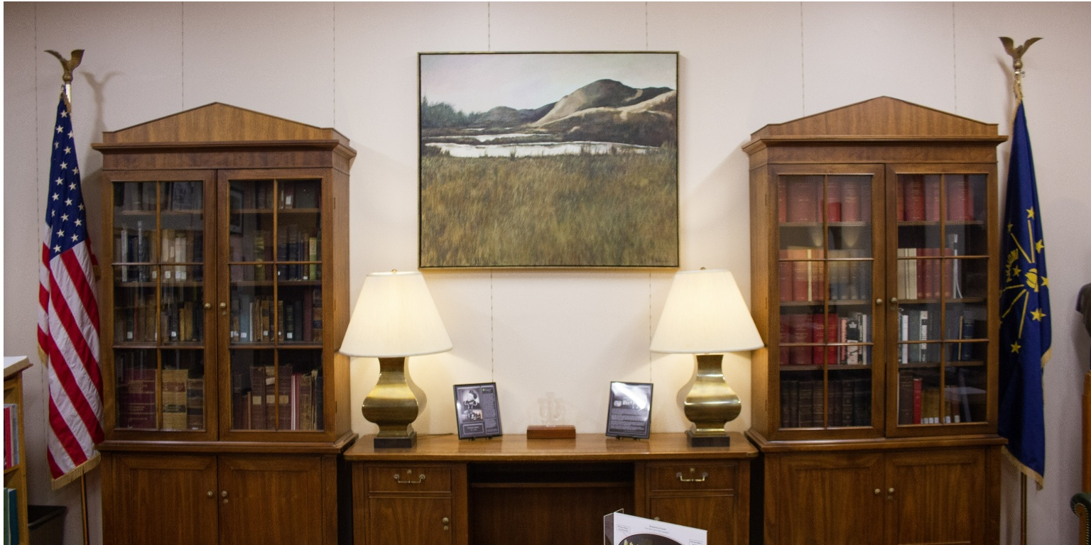 A bookcase and desk with a painting on the wall in the middle and a flag on each side.