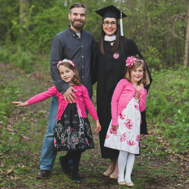 A woman in a cap and gown stands smiling with her family.