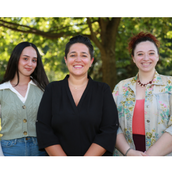 A faculty member and two students smile in front of trees.