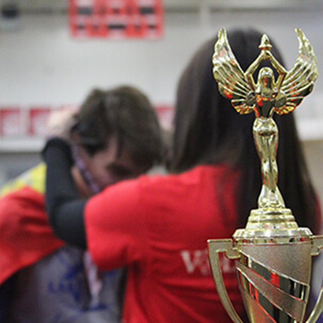 A golden trophy with a student receiving a medal in the background.