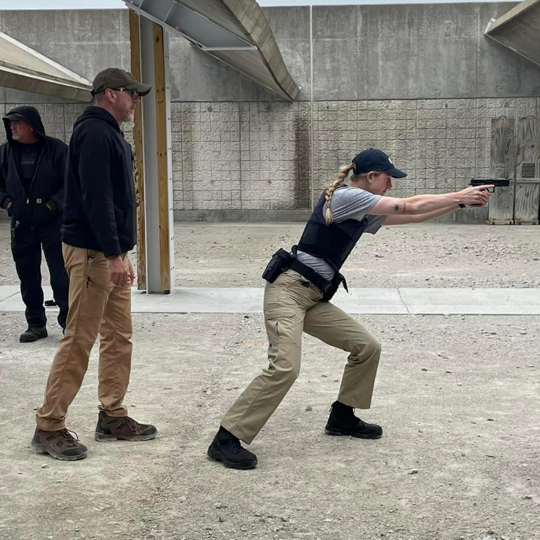 A female student points a firearm to her right with an instructor behind her.